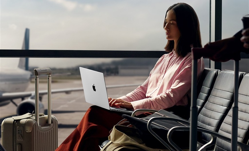 Jak vybrat notebook? žena sedí v letištní hale na lavičce a pracuje na MacBooku Pro 14 M5, který má položen na kolenou